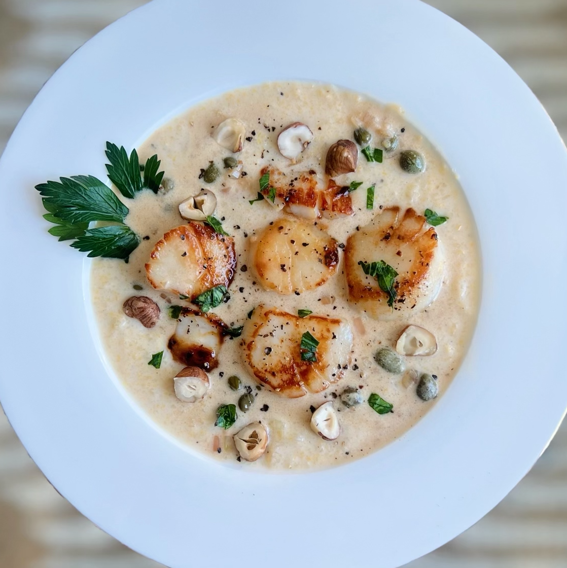 Seared Alaska Weathervane scallops seared and served in a bowl with creamy polenta, parsley, and capers