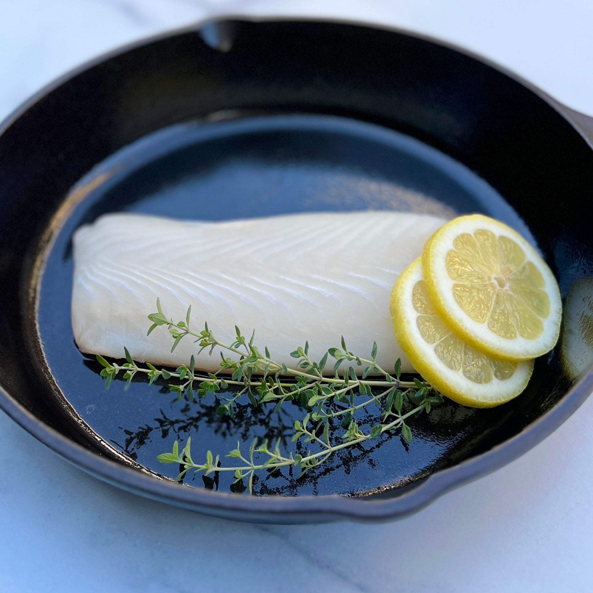 Raw halibut fillets in a cast-iron skillet.