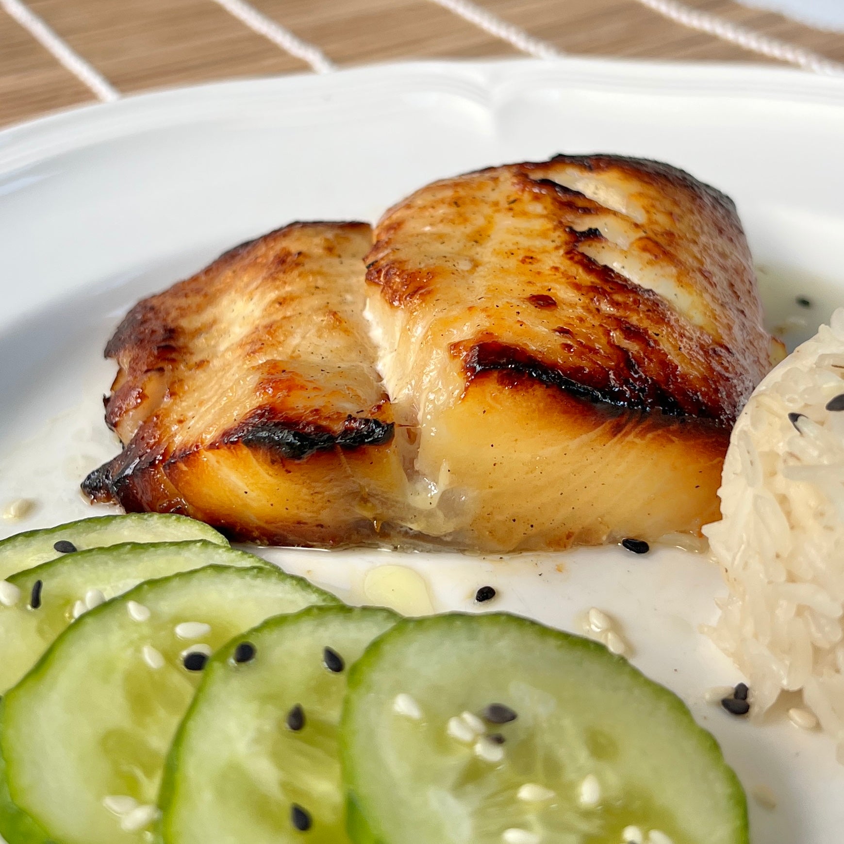 Broiled miso-marinated black cod served on a plate with sliced cucumbers and rice