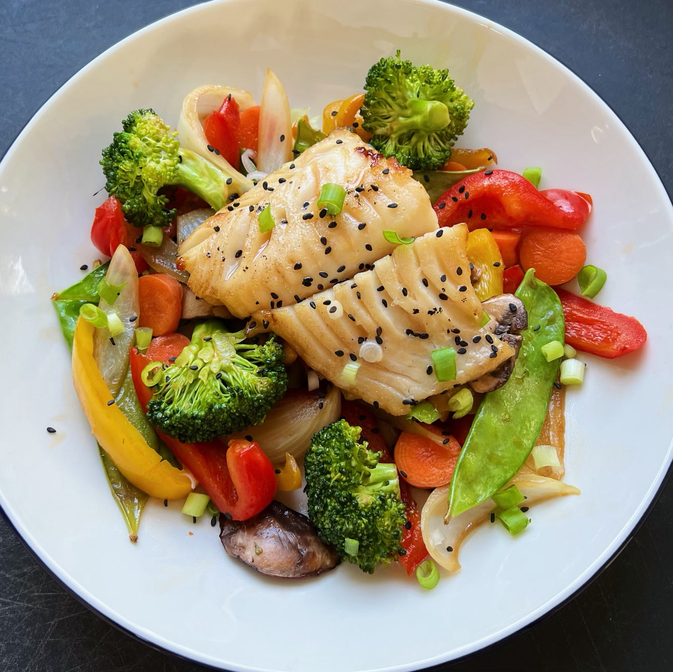 Miso marinate black cod served on a plate with assorted peppers, mushrooms, and other vegetables