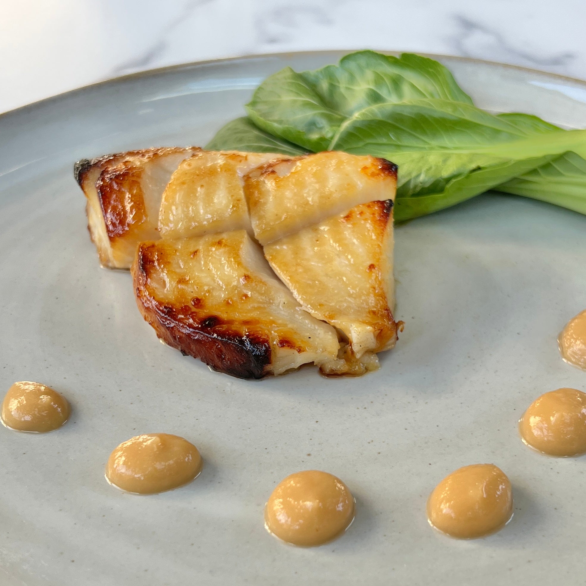 Grilled miso-marinated black cod served Nobu-style on a plate with bok choy and yum yum sauce